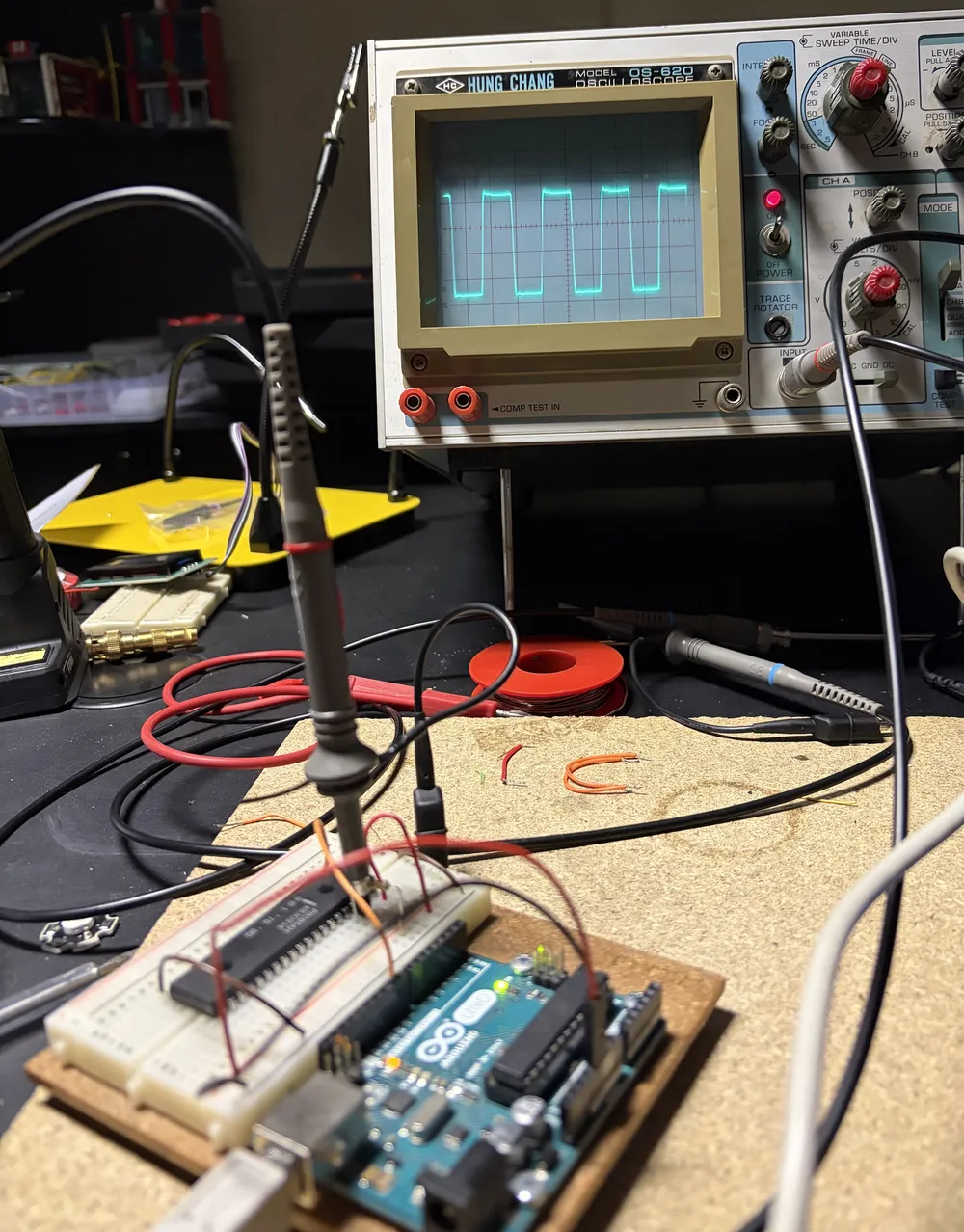 The 8085 on a breadboard next to an Arduino Uno, with an oscilloscope in the background showing a square wave clock signal