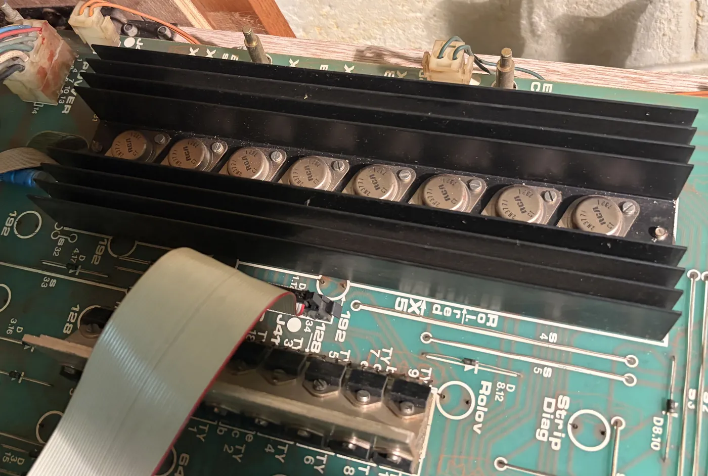 The lamp board with a long black heatsink holding a row of eight metal-can power transistors