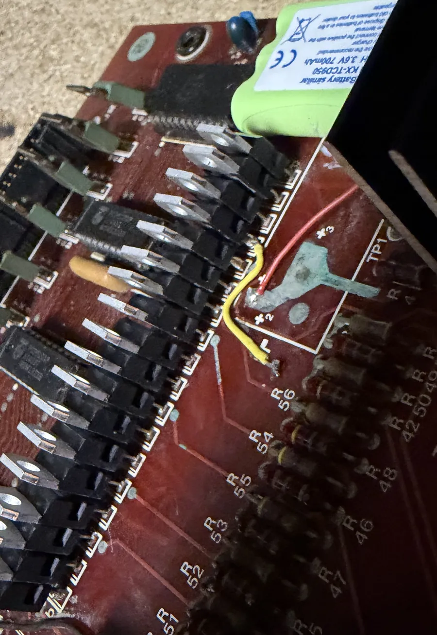 Corner of the CPU board with a row of new black darlington transistors, a damaged trace bridged with red and yellow wires, and the new green NiMH battery pack